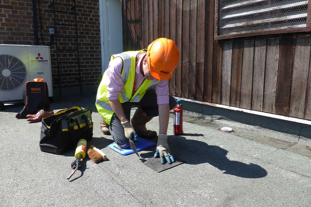 Technician in hi vis and hard hat core sampling a flat roof